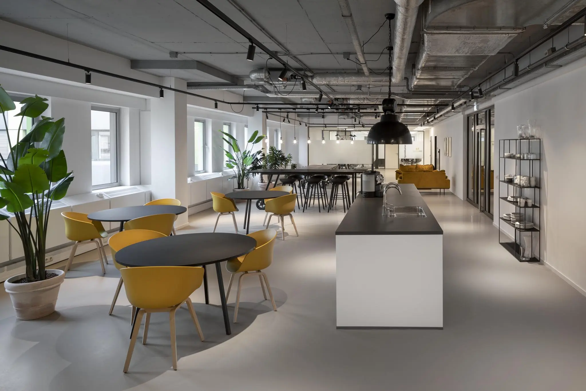 Moderne kantoorruimte aan de Van Boshuizenstraat met open keuken, gele stoelen, zwarte tafels en veel natuurlijke lichtinval.